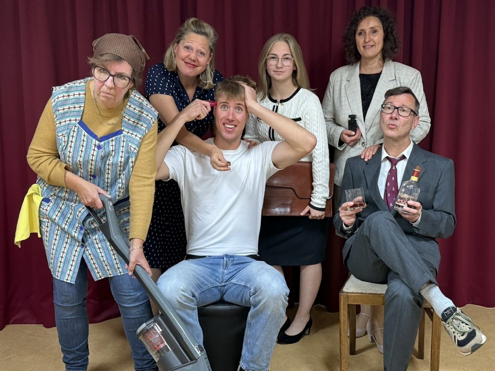 Job suey: Ensemble vor dem roten Vorhang (Querformat) Job suey: Das Ensemble vor dem roten Vorhang – Putzfrau mit Staubsauger, Jim Watt in der Mitte, sein Chef mit Whiskyglas
