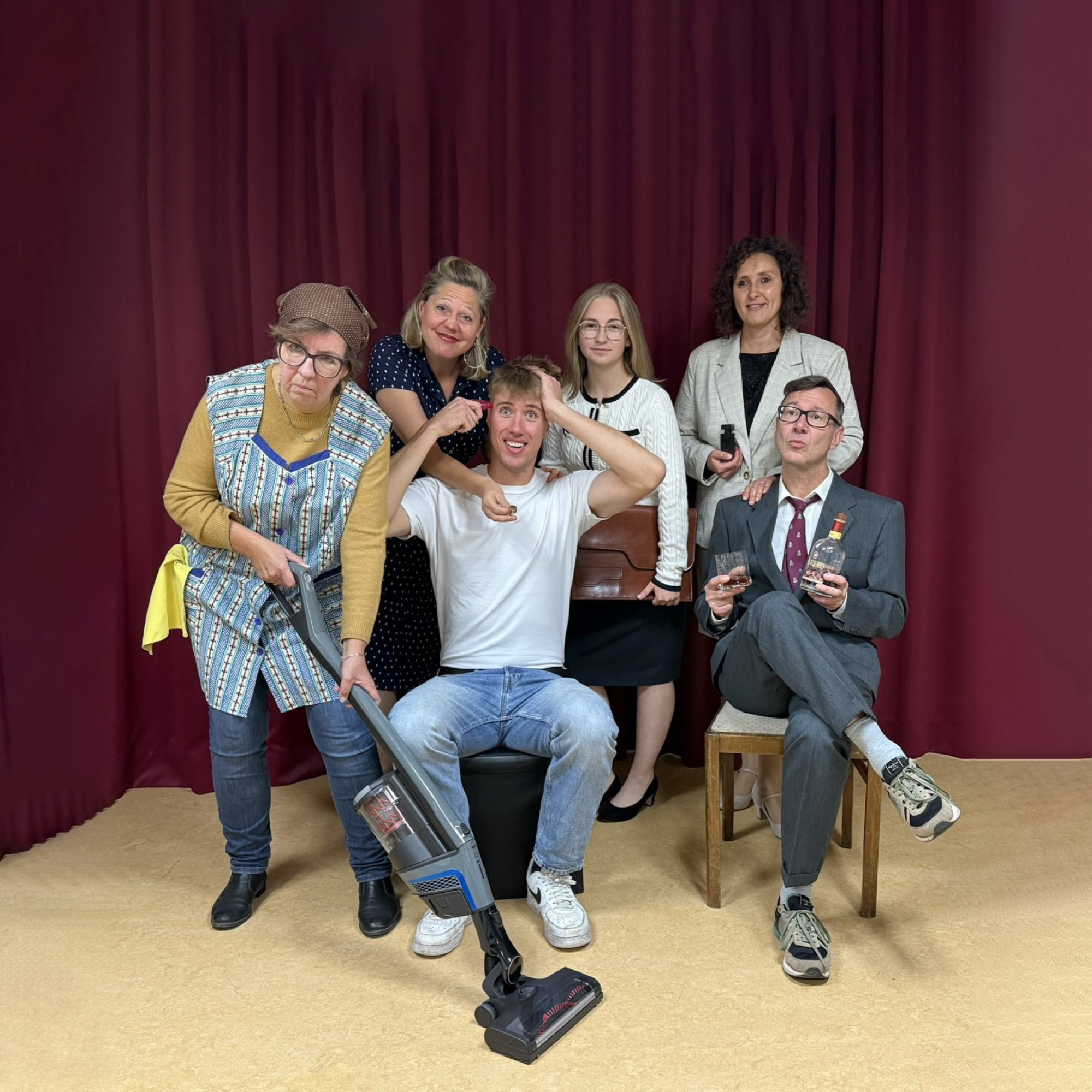 Job suey: Ensemble mit Staubsauger, Whisky und Aktentasche vor dem roten Vorhang (quadratisch) Job suey: Das Ensemble vor dem roten Vorhang – Putzfrau mit Staubsauger, Jim Watt in der Mitte, sein Chef mit Whiskyglas